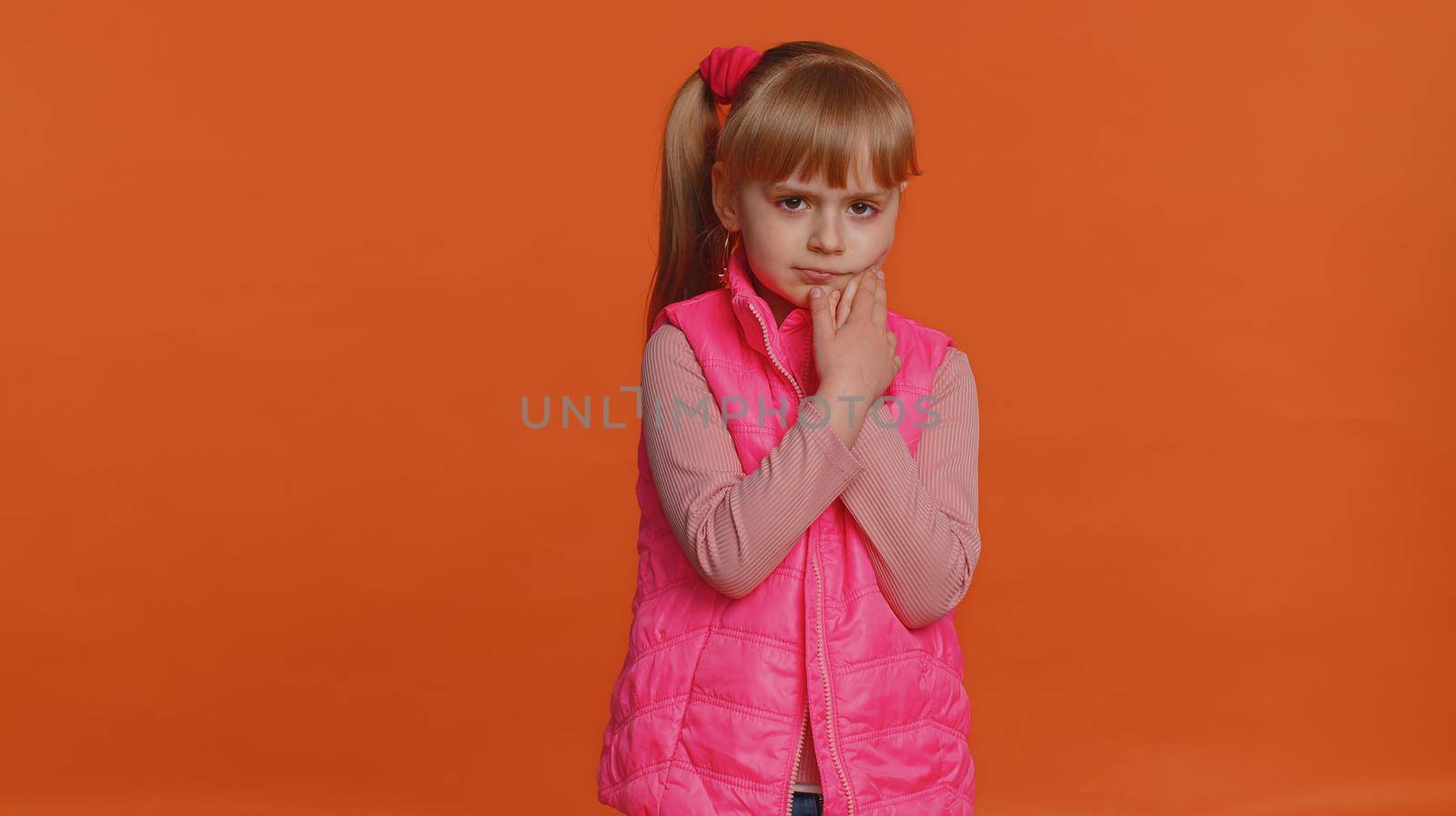 Toddler young girl touching sore cheek suffering from toothache cavities or gingivitis waiting for dentist appointment, gums disease. Little child indoors isolated alone on orange studio background