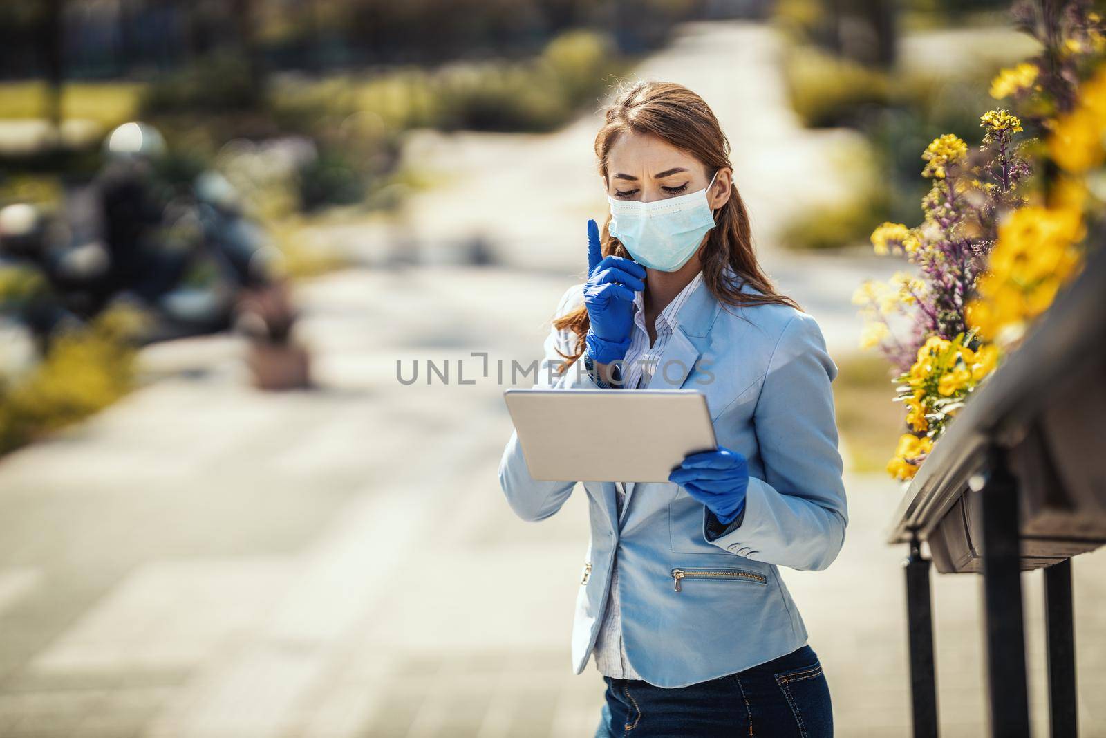 Young business woman with protective mask on her face is looking something on her digital tablet outdoors.