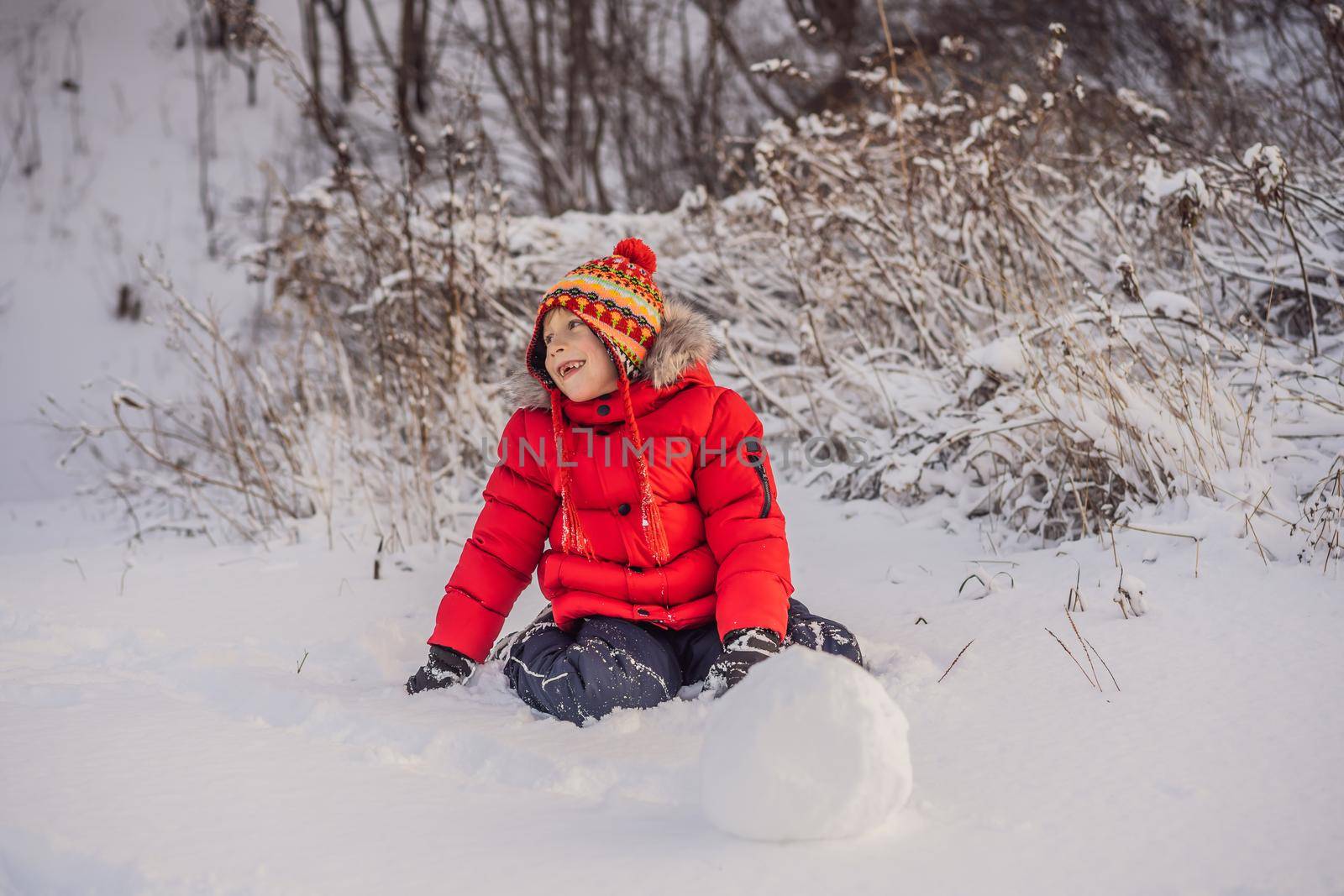 Cute boy in red winter clothes builds a snowman. Winter Fun Outdoor Concept.