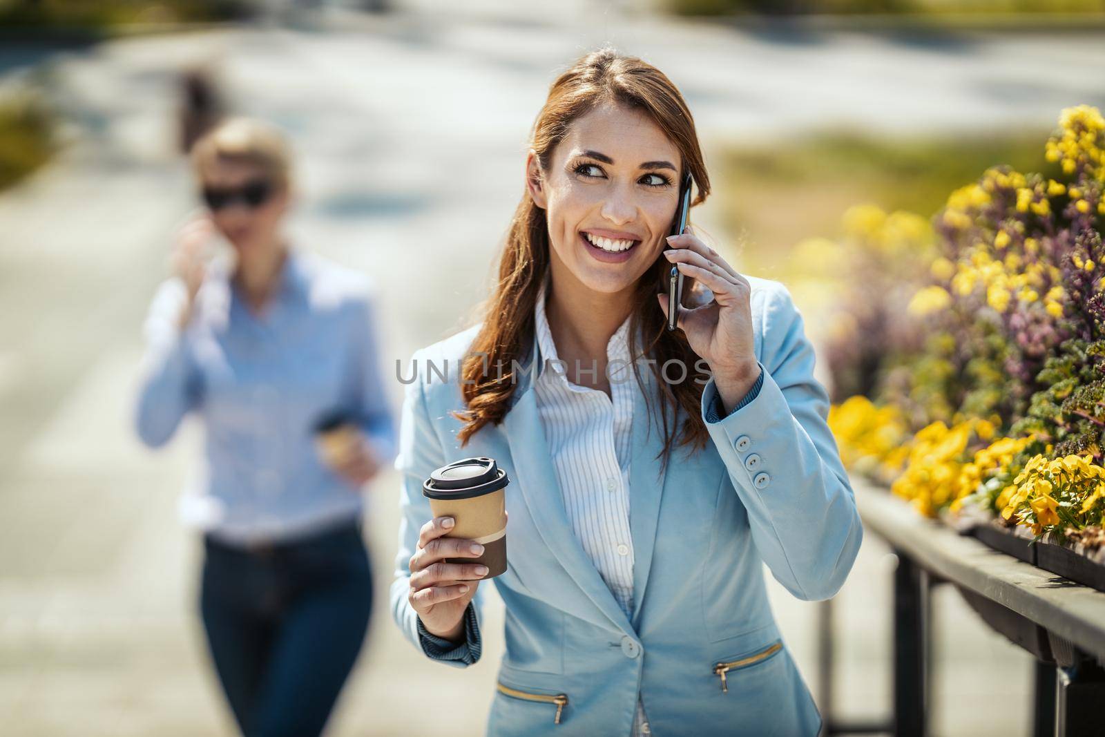 Young smiling businesswoman is walking in front of office and talking on the smartphone during coffee break.