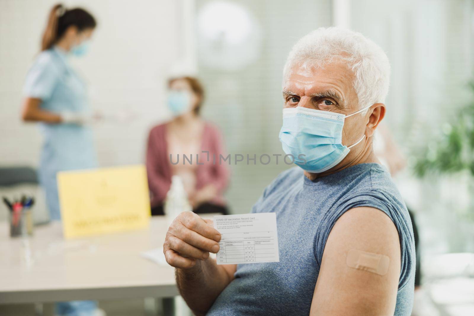 A senior man showing vaccination certificate after receiving the Covid-19 vaccine. Looking at camera.
