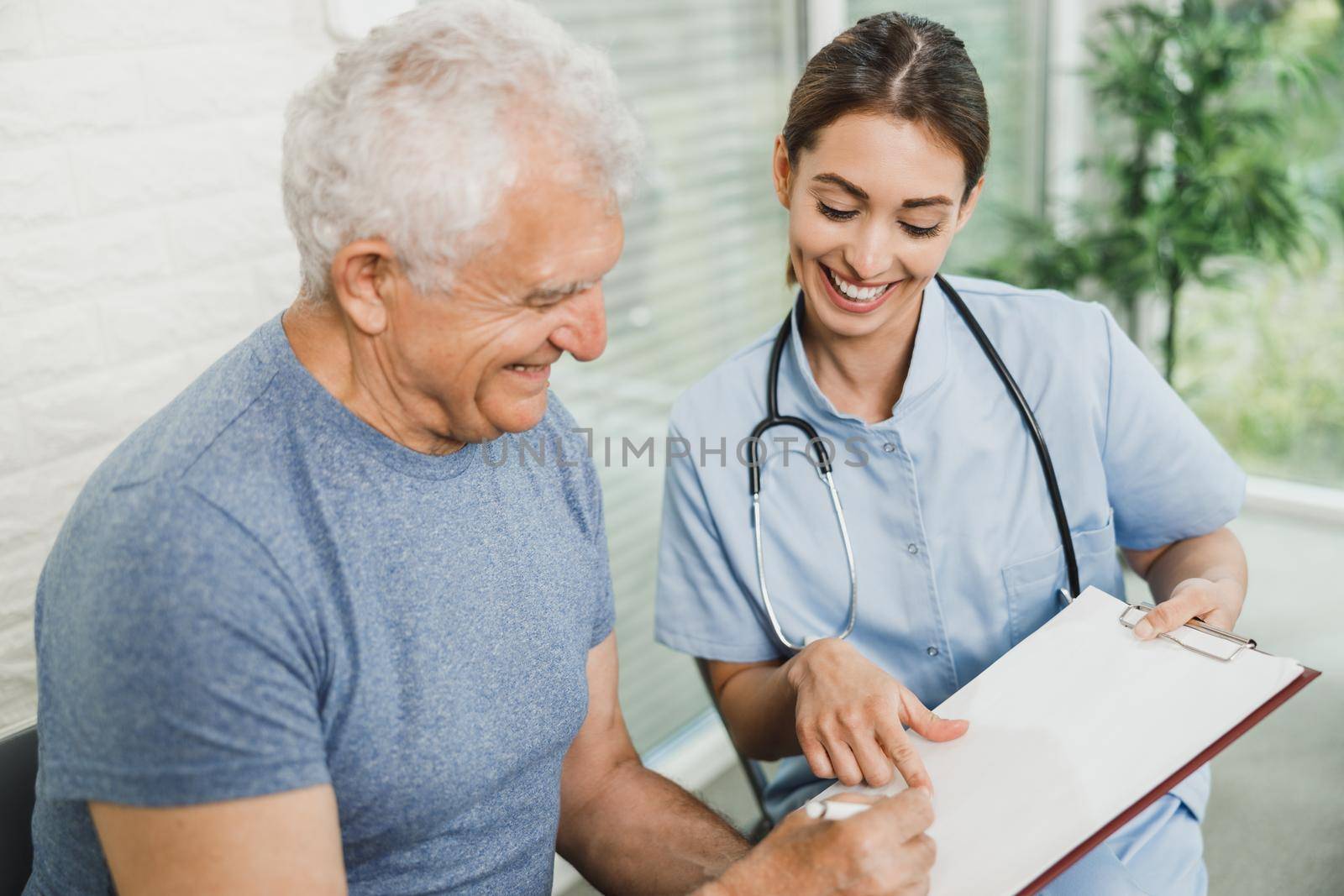 Senior Man Talking To Nurse At Waiting Room by MilanMarkovic78