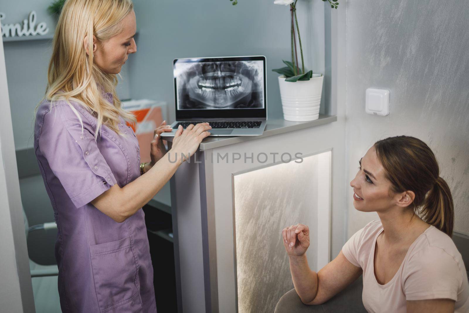 An attractive young woman sitting in waiting room and having a consultation with her dentist.