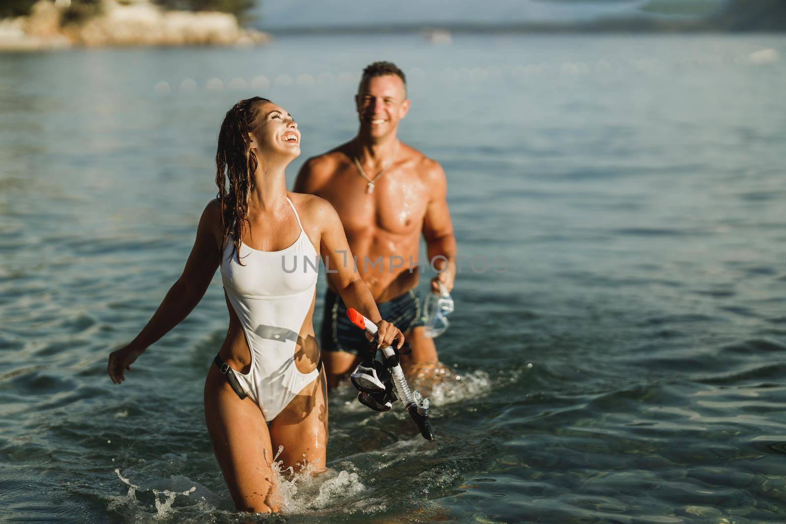 A cheerful couple with their scuba masks and snorkels walking through the sea after snorkeling.