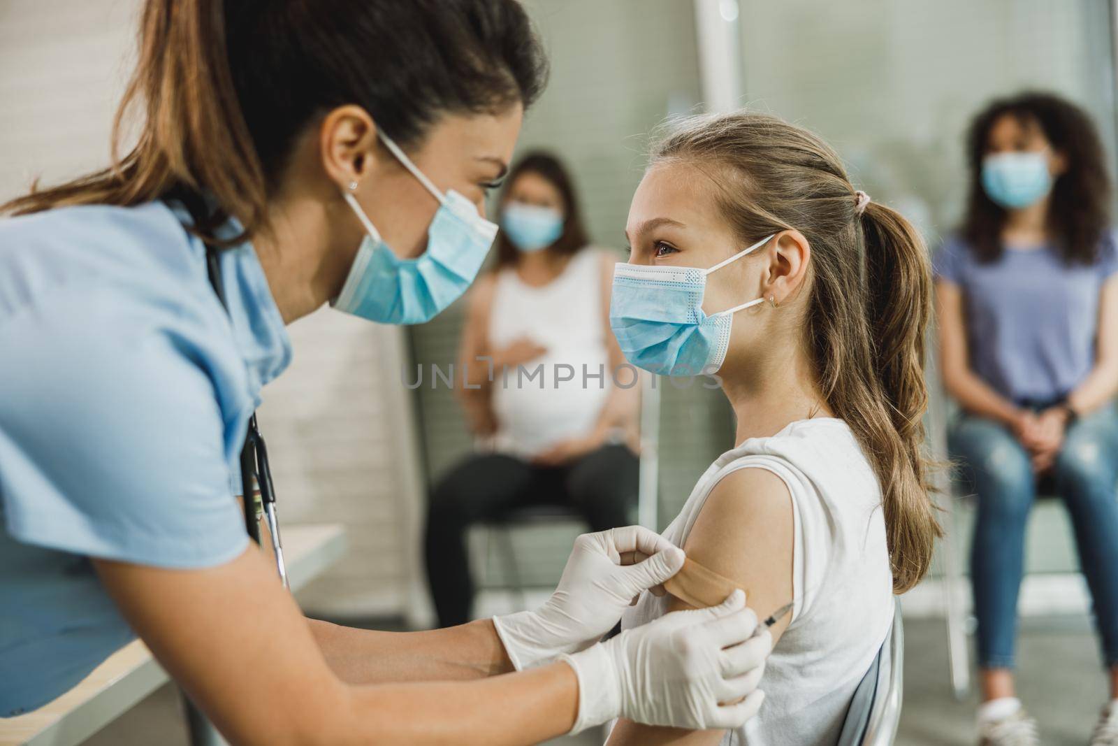 A nurse applying a band aid to a cute teenager girl after receiving the Covid-19 vaccine.