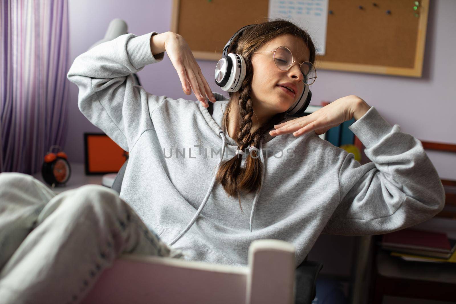A teen raises her hands while listening to music. Musical emotion is translated into verbal emotion. A young girl with braids and glasses listens to music.