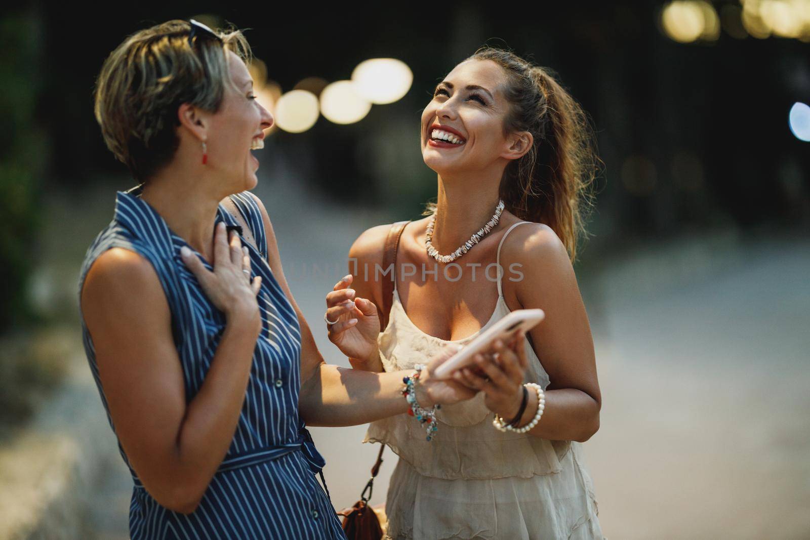 Two cheerful young women are having fun and using a cellphone together while enjoying a summer vacation.