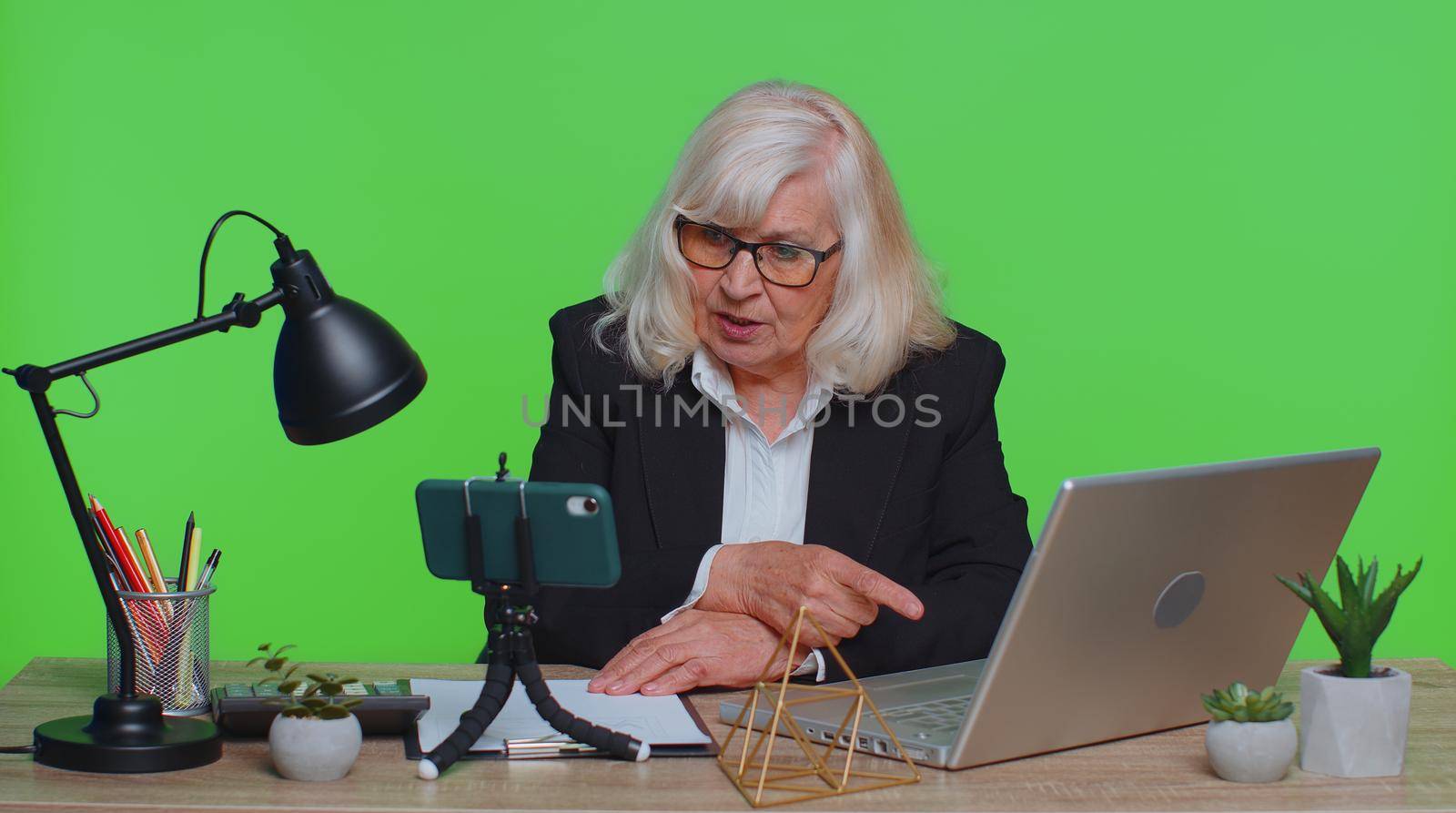 Senior businesswoman blogger making mobile phone conference video call vlog. Elderly professional call center agent, operator having distance smartphone webcam chat job interview on computer in office