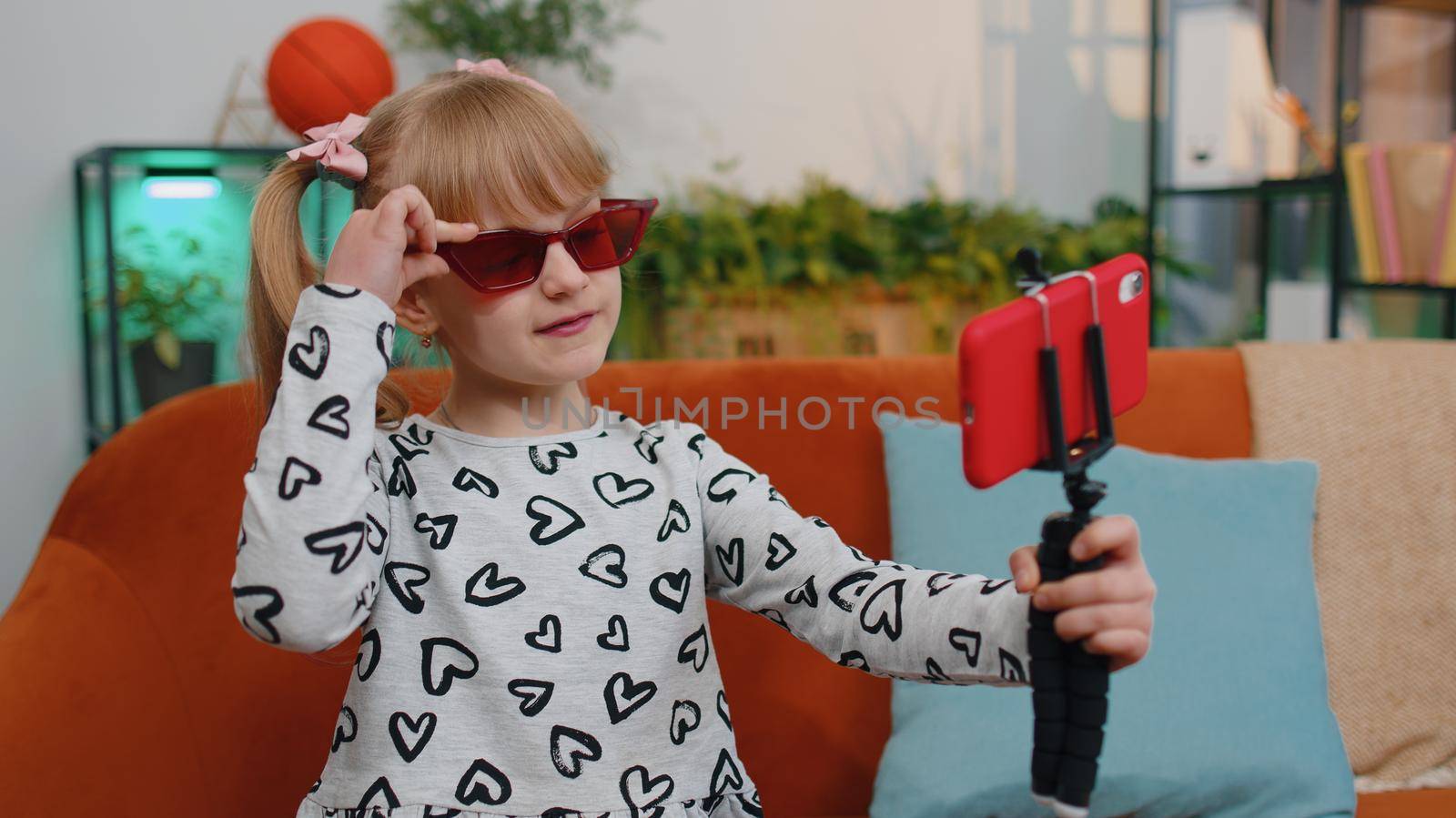 Portrait of Caucasian little happy child girl enjoying conversation on mobile phone with friend relaxing sitting on couch in living room. School toddler kid at home alone. Communication teens concept