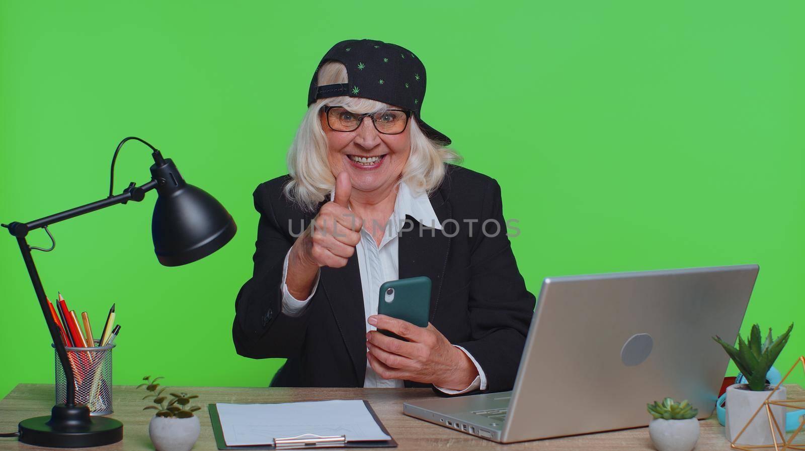 Happy excited funny stylish senior businesswoman use smartphone typing browsing say wow yes, great big win good news shocked by sudden victory at office. Elderly woman on chroma key studio background