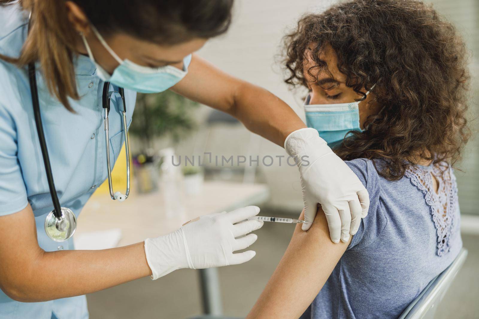 A nurse giving a vaccine to African American teenager girl due to coronavirus pandemic.
