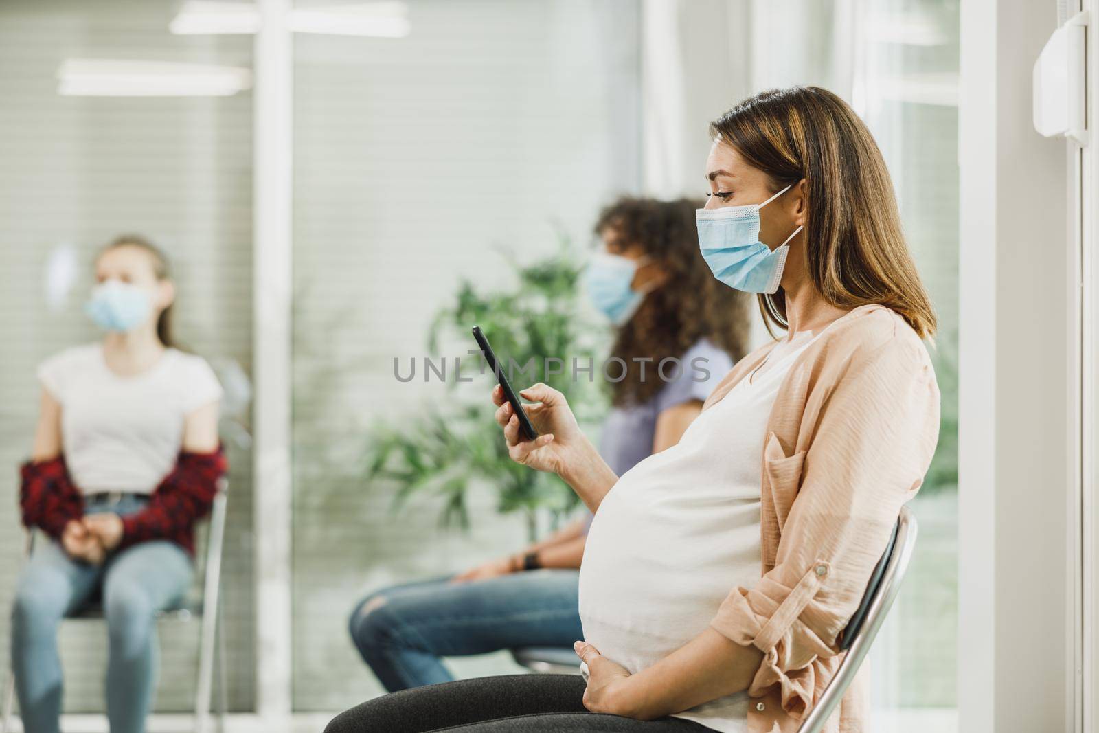 Pregnant Woman Using Smartphone At The Waiting Room by MilanMarkovic78