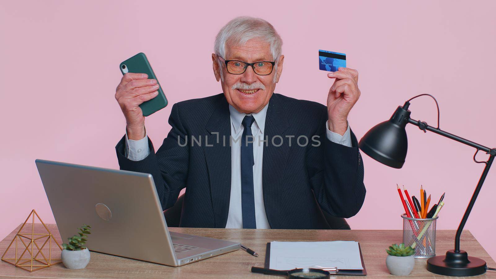 Senior businessman use smartphone and plastic credit bank card, browsing say wow yes, found out great big win, success lotter, good news, purchases online shopping. Elderly man on pink background