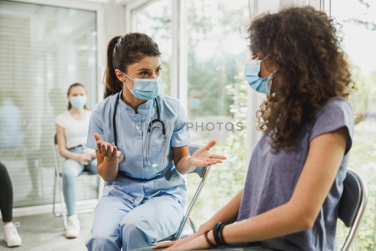 Nurse talking to African American teenage girl before vaccination against coronavirus at waiting room.