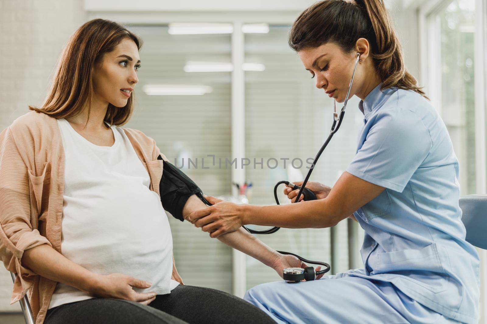 Gynecology nurse talking to pregnant woman and checking the blood pressure to her.