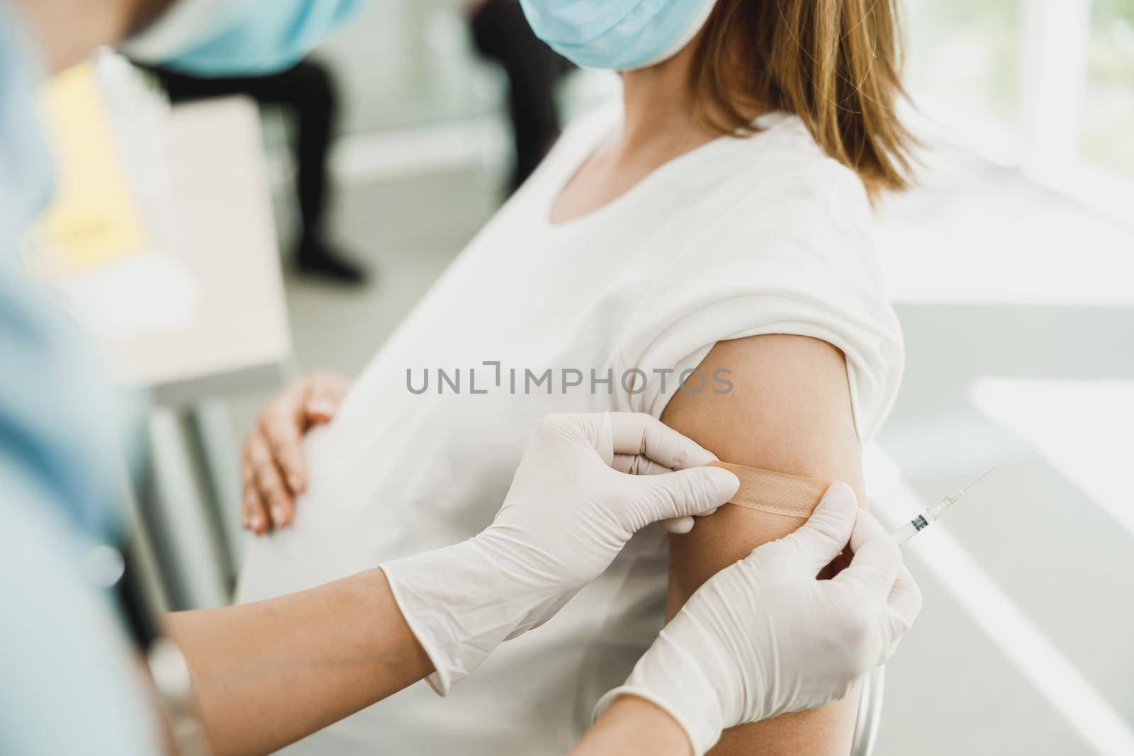 Close-up of a nurse applying a band aid to a young pregnant woman after receiving a vaccine due to coronavirus epidemic.