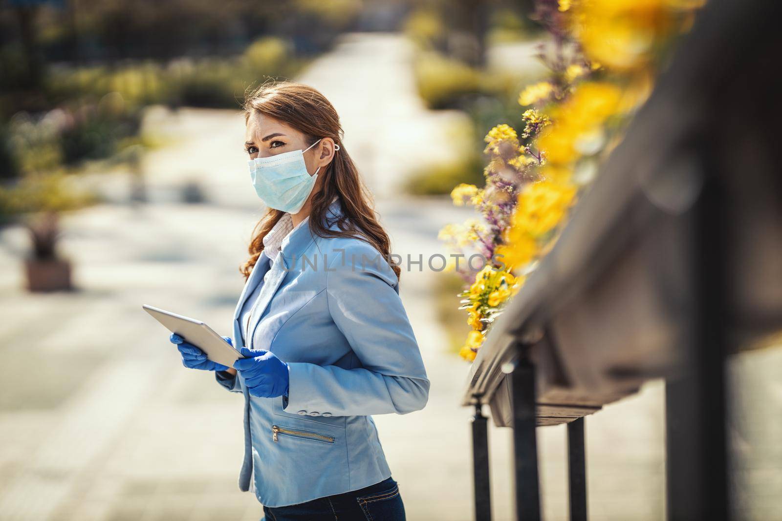 Young business woman with protecting mask on her face is looking something on her digital tablet outdoors.