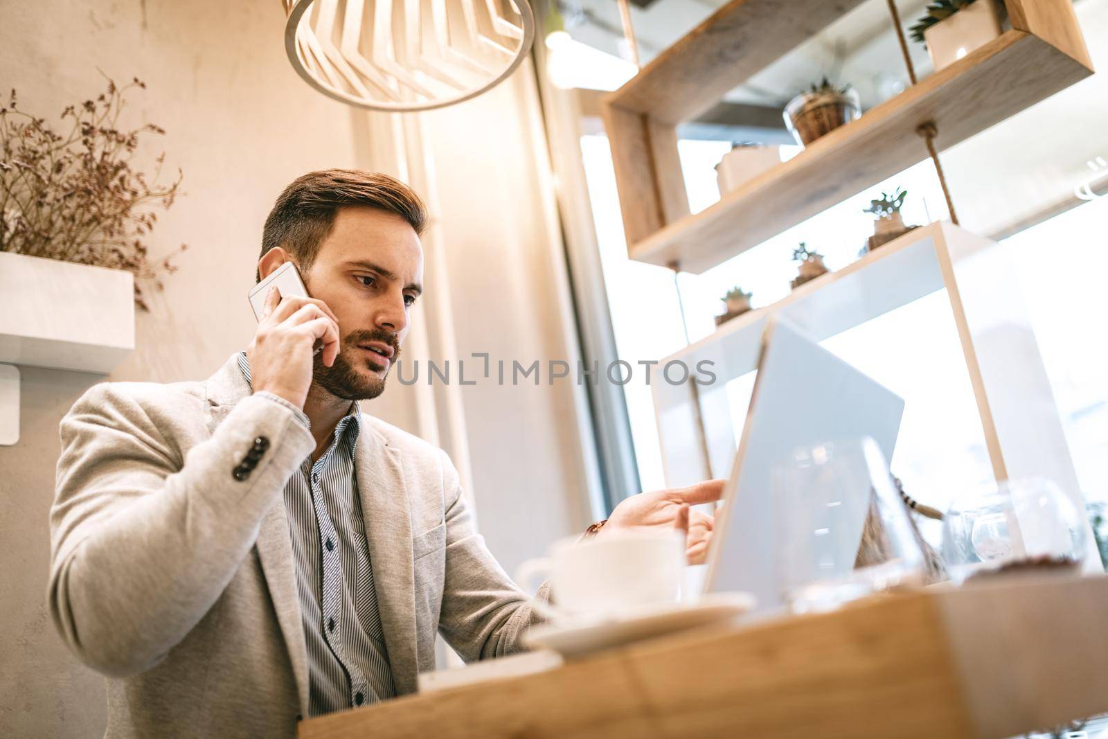 Young businessman on a break in a cafe. He is working at laptop and using smartphone. 