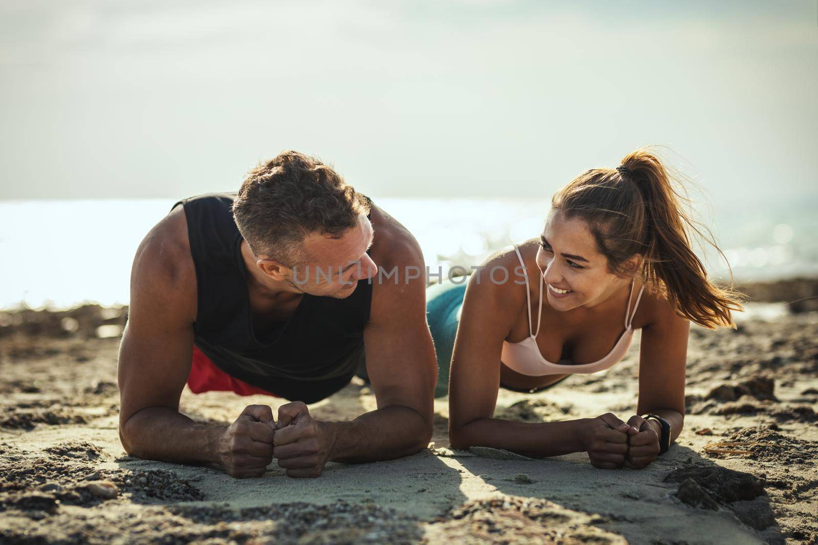 A beautiful couple is doing push-up exercises at the sea beach in summer sunny day.