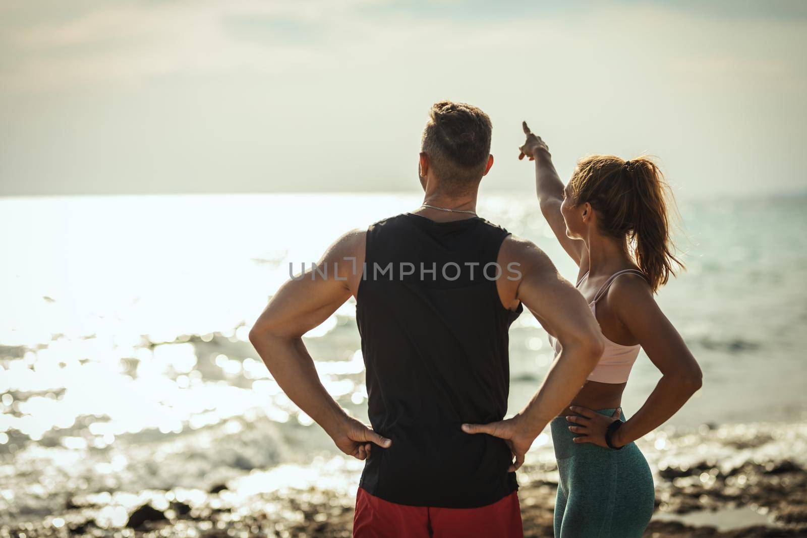 A beautiful young woman and handsome man are relaxing during training at the sea beach in summer sunny day.