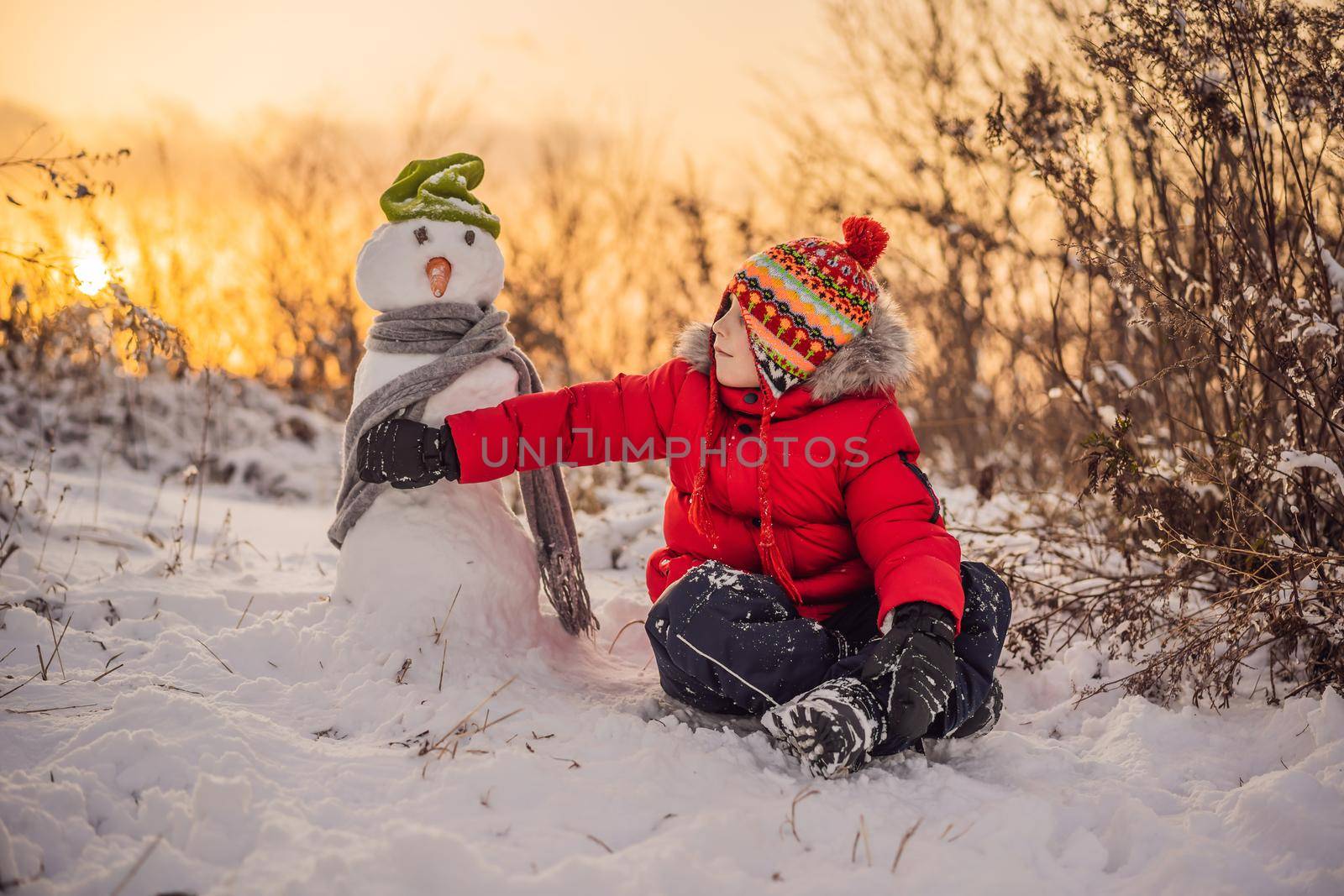 Cute boy in red winter clothes builds a snowman. Winter Fun Outdoor Concept.