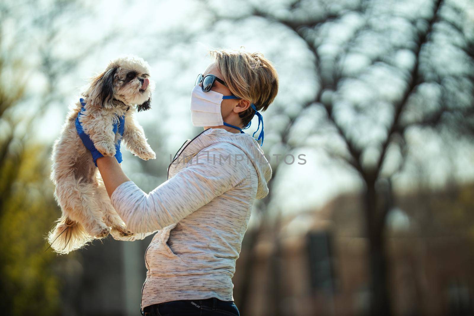 A woman in a medical protective mask is spending time with her dear cute little Shih Tzu dog on the city street path during flu virus outbreak and coronavirus epidemic.