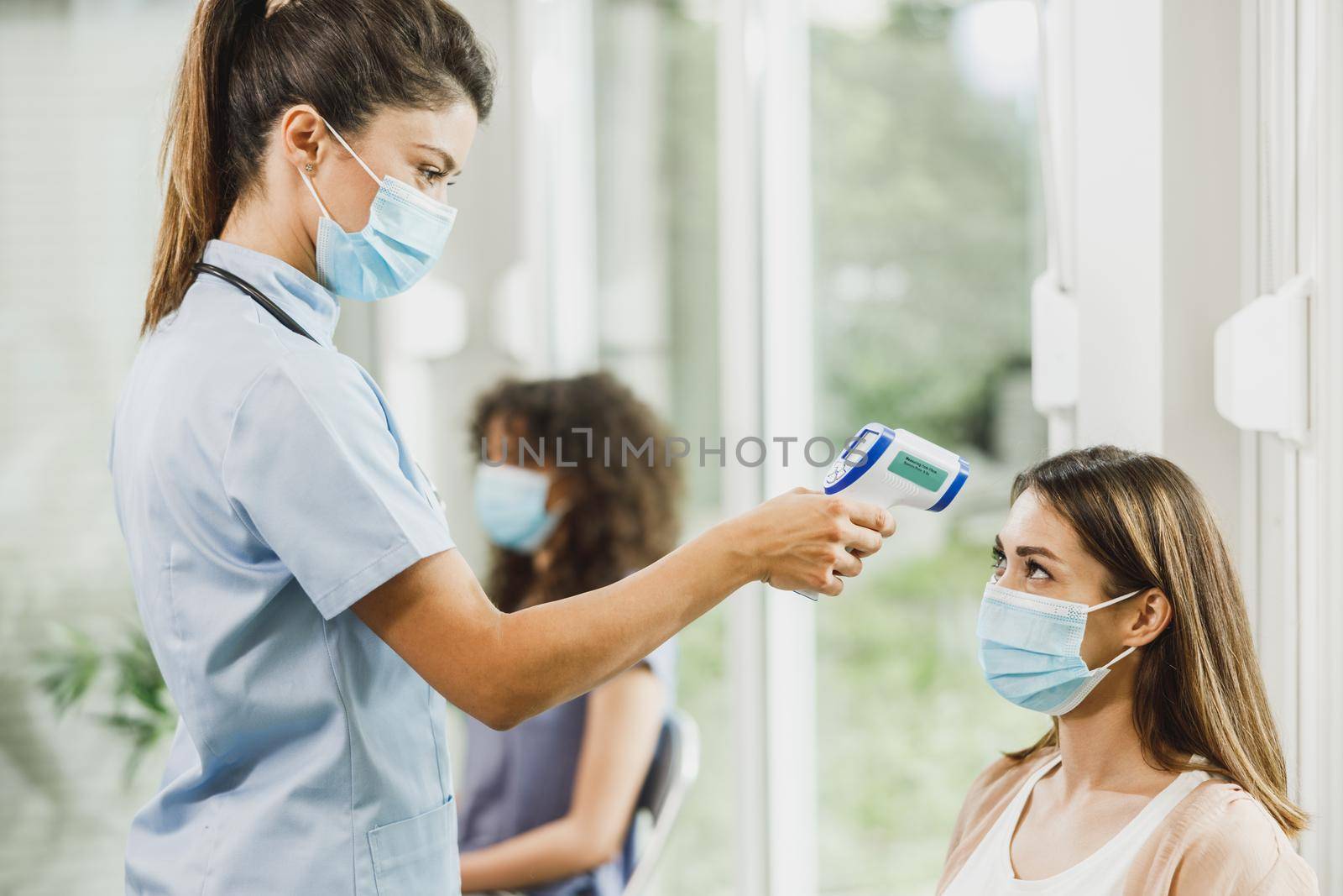 Young woman with a face mask having her temperature checked before coronavirus vaccine.