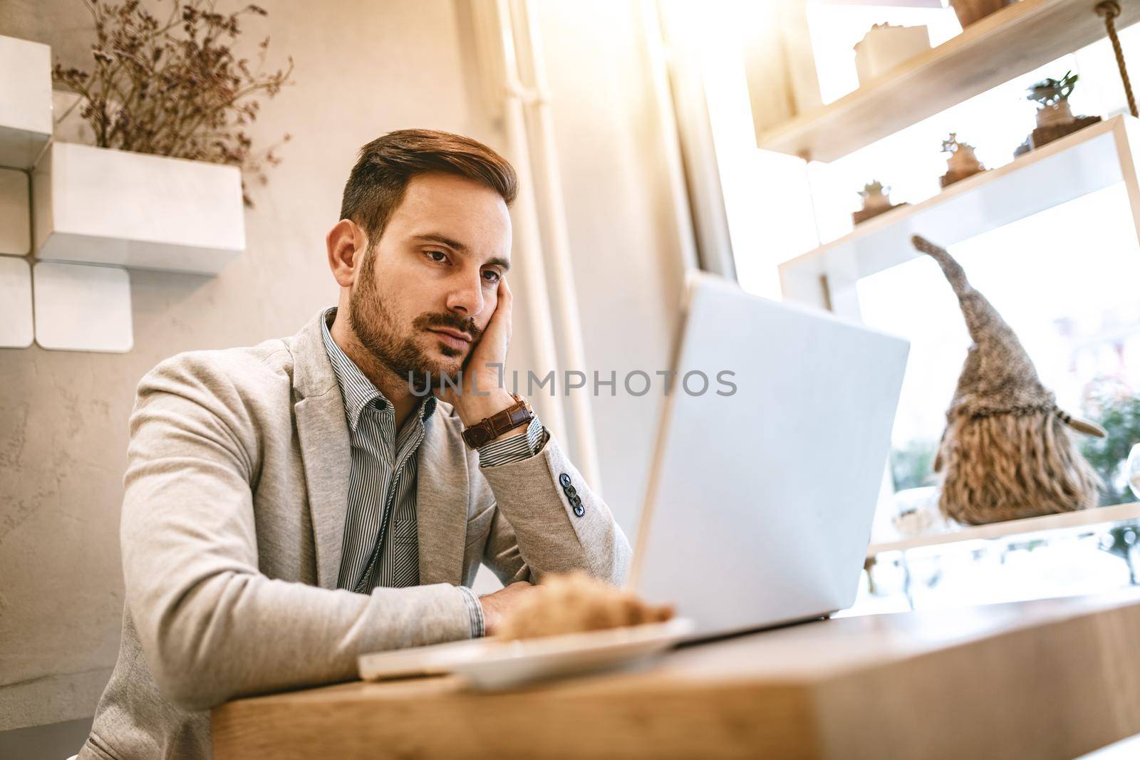 Young pensive businessman on a break in a cafe. He is working at laptop and thinking. 