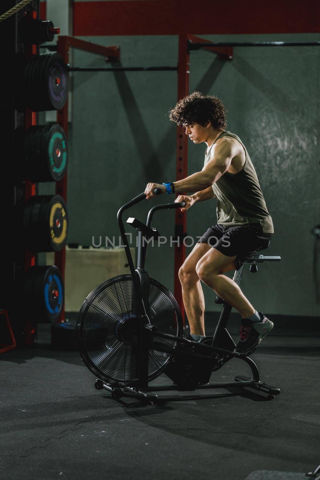 A young muscular man is doing hard cal bike crossfit training in the gym.