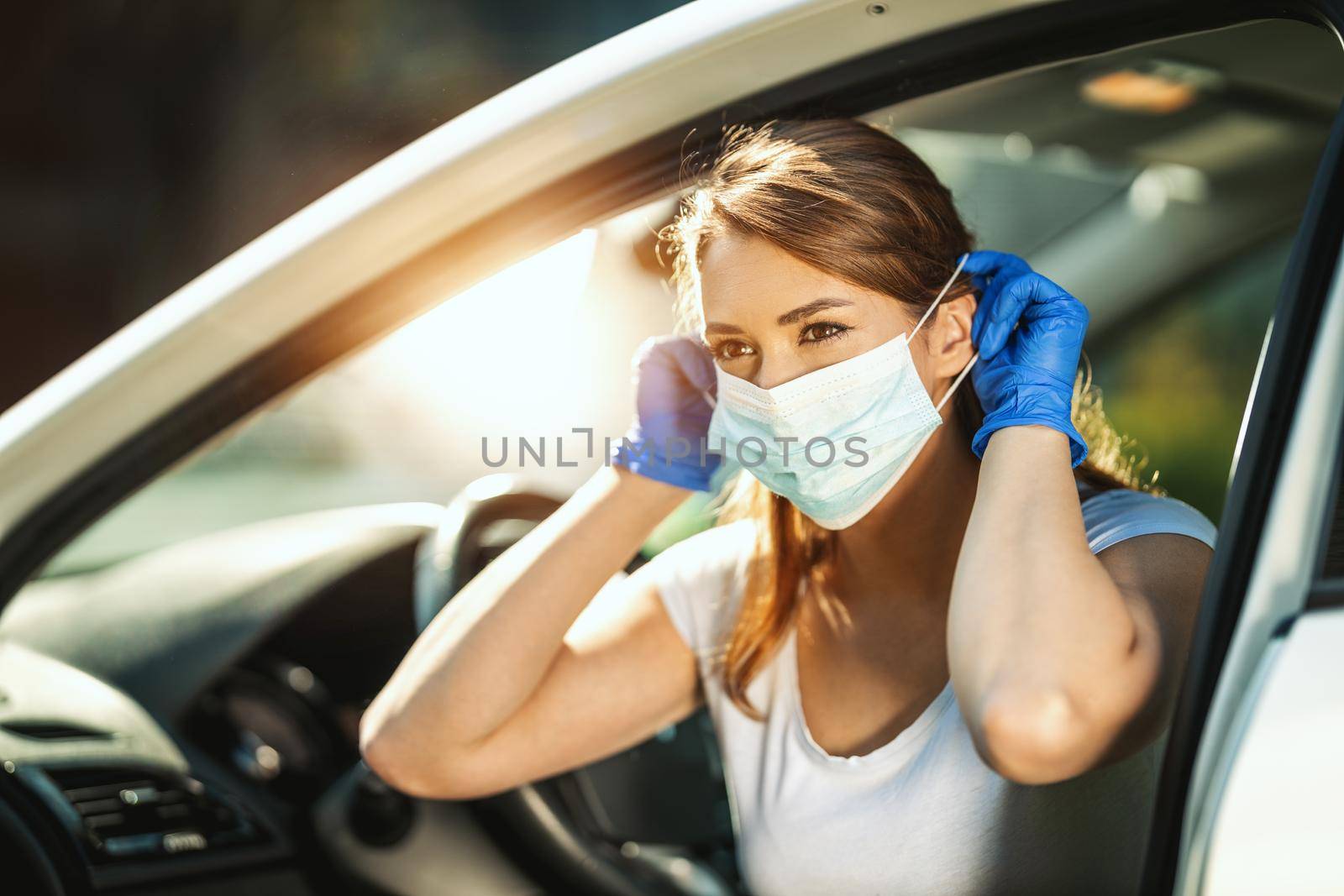 A young woman is putting a mask on her face, to avoid infection during flu virus outbreak and coronavirus epidemic, getting ready to go to work by car.