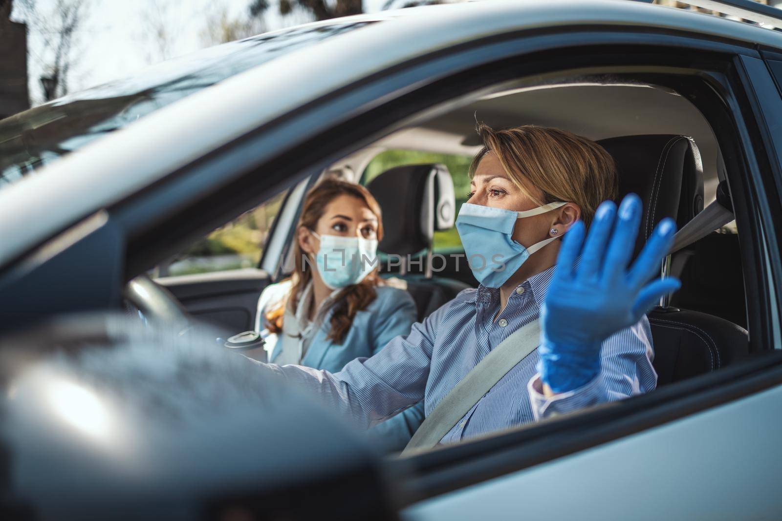 Young business women with protective masks on their faces are going to the work together by car and talking about global crisis. 
