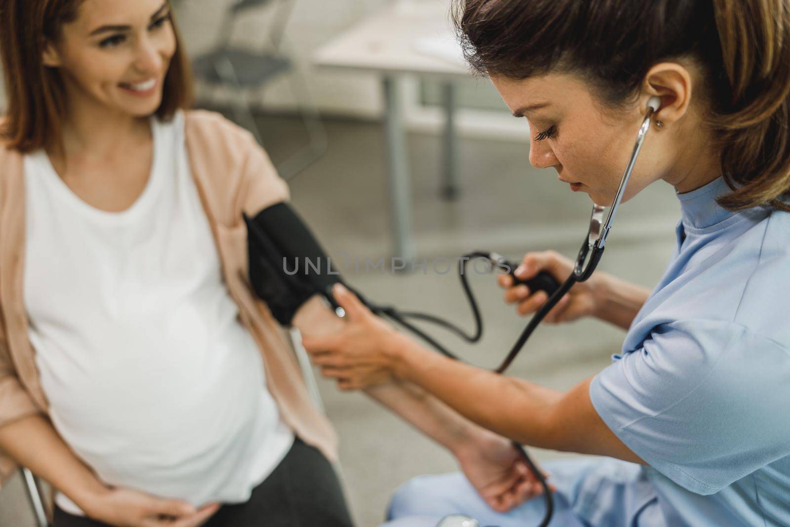 Close-up of a gynecology nurse talking to pregnant woman and checking the blood pressure to her.