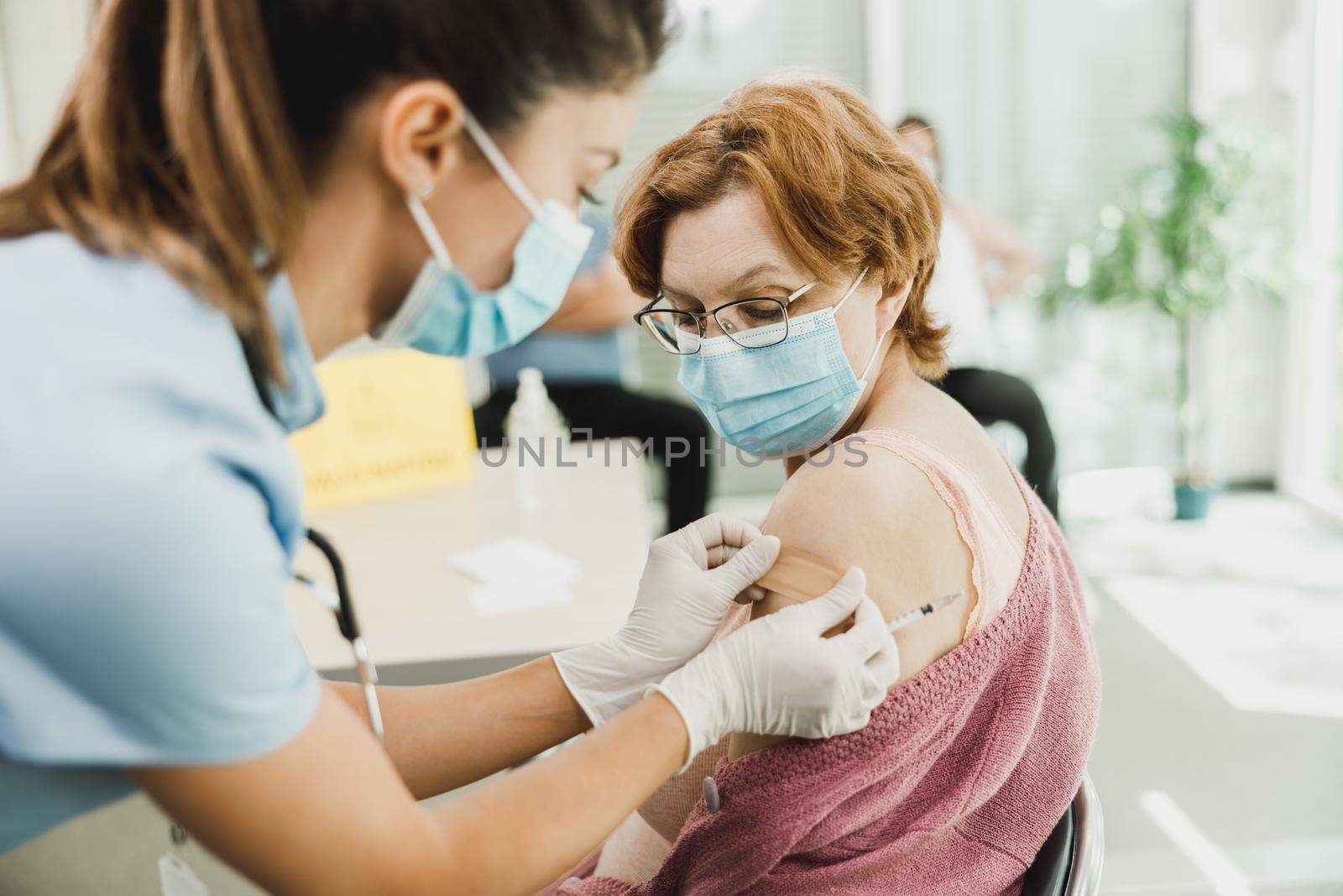 A nurse applying a band aid to a senior woman after receiving a vaccine due to coronavirus epidemic.
