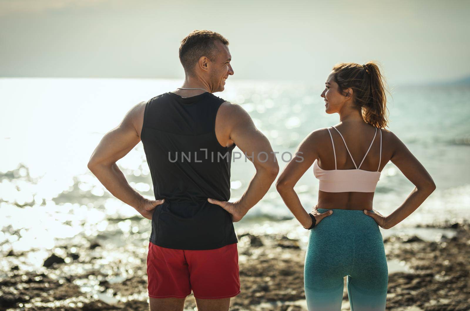 A beautiful young woman and handsome man are ready to do stretching exercise by the sea in sunrise.