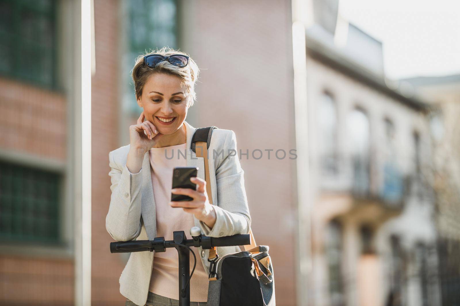 A mature businesswoman surfing net on a smartphone while going to work with an electric scooter.
