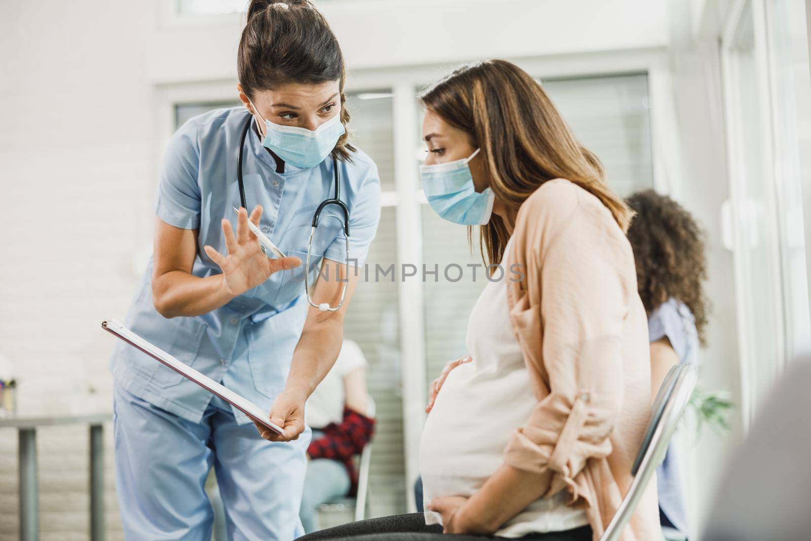 Nurse talking to young pregnant woman and analyzing medical report before before vaccination against coronavirus.