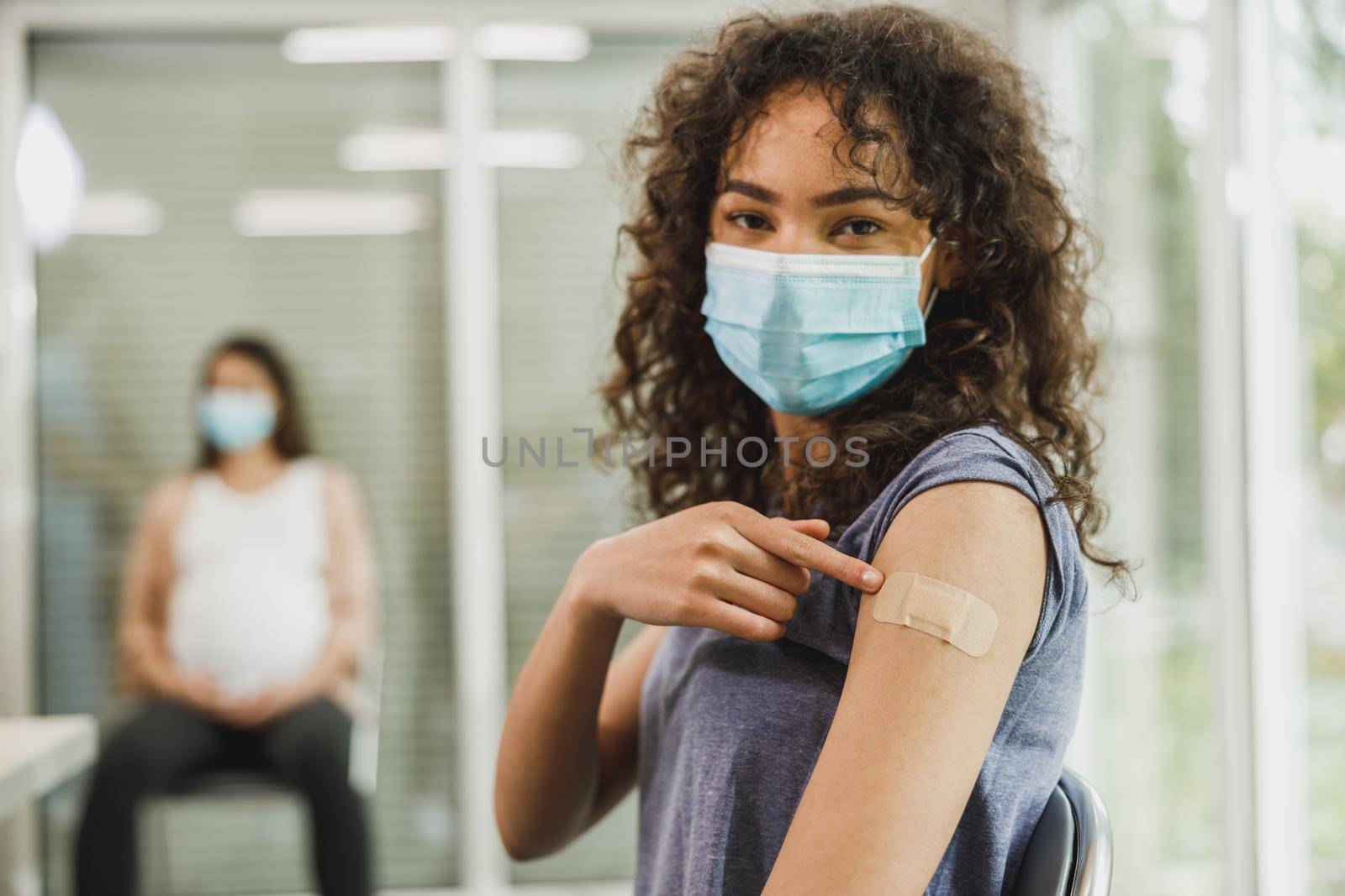An African American teenager girl showing at her arm with a band aid after receiving the Covid-19 vaccine.