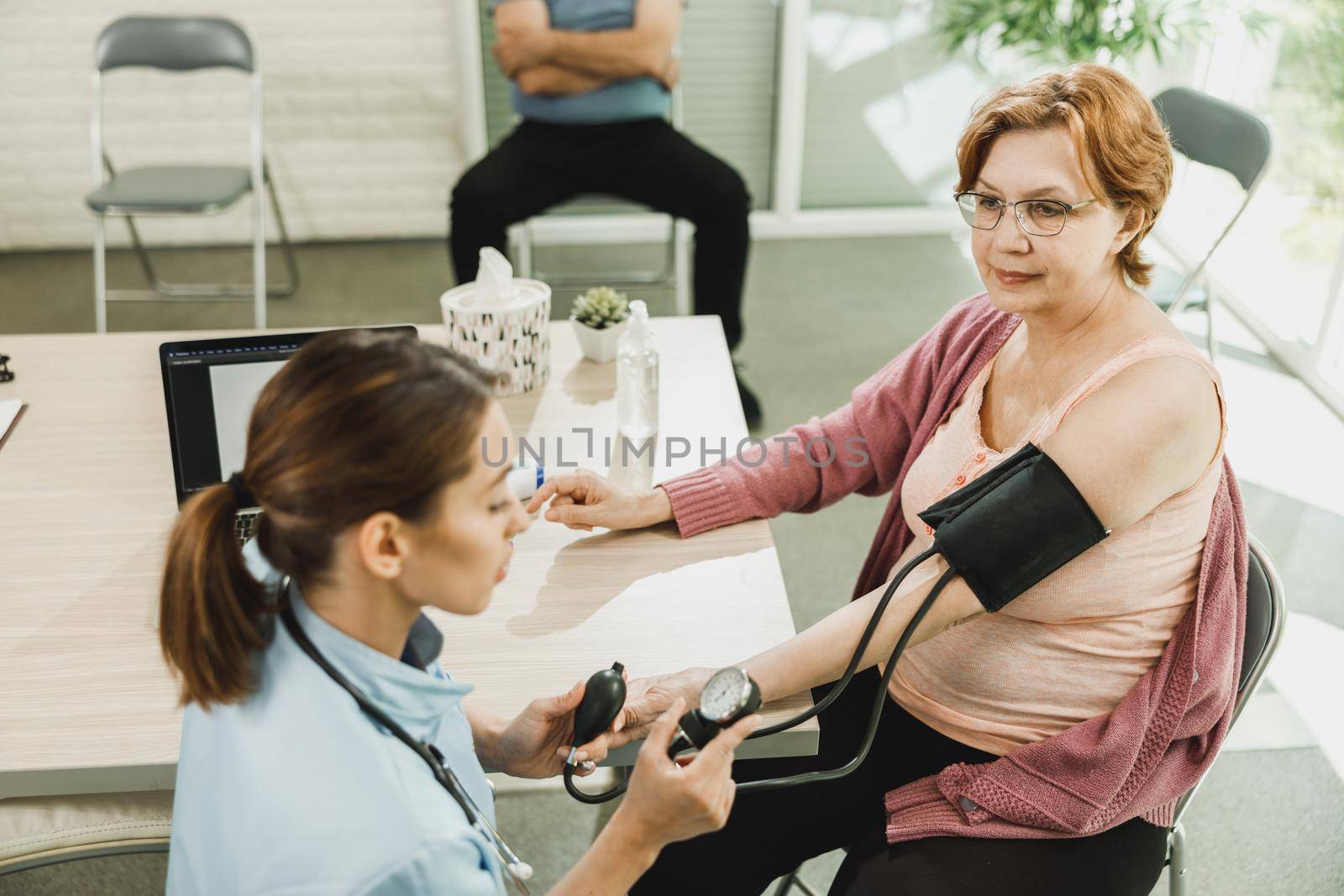 Nurse talking to senior woman and checking the blood pressure to her.