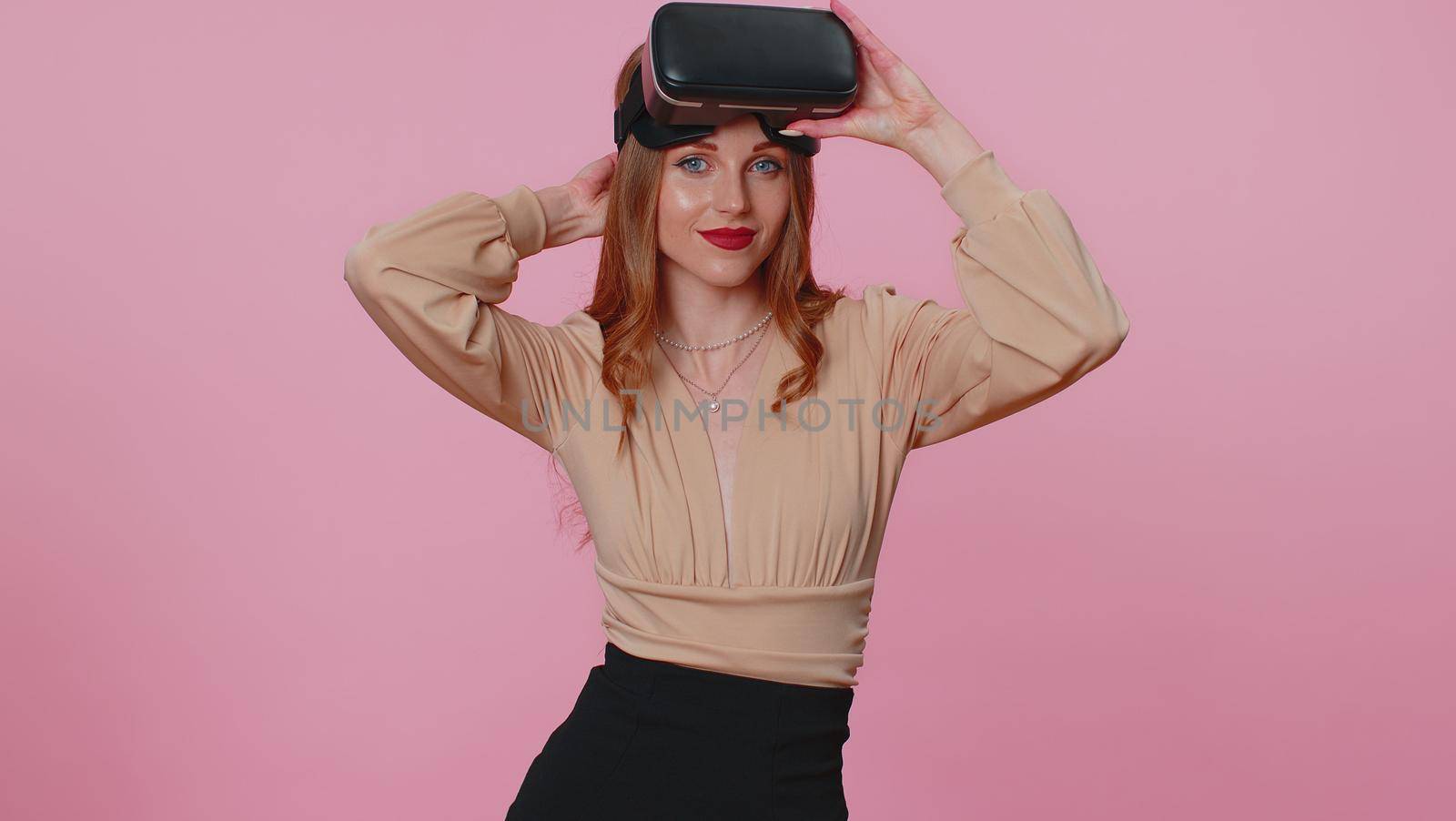 Teen brunette girl using virtual reality futuristic technology VR app headset helmet to play simulation 3D 360 video game, drawing. Young woman on pink studio background. People sincere emotions