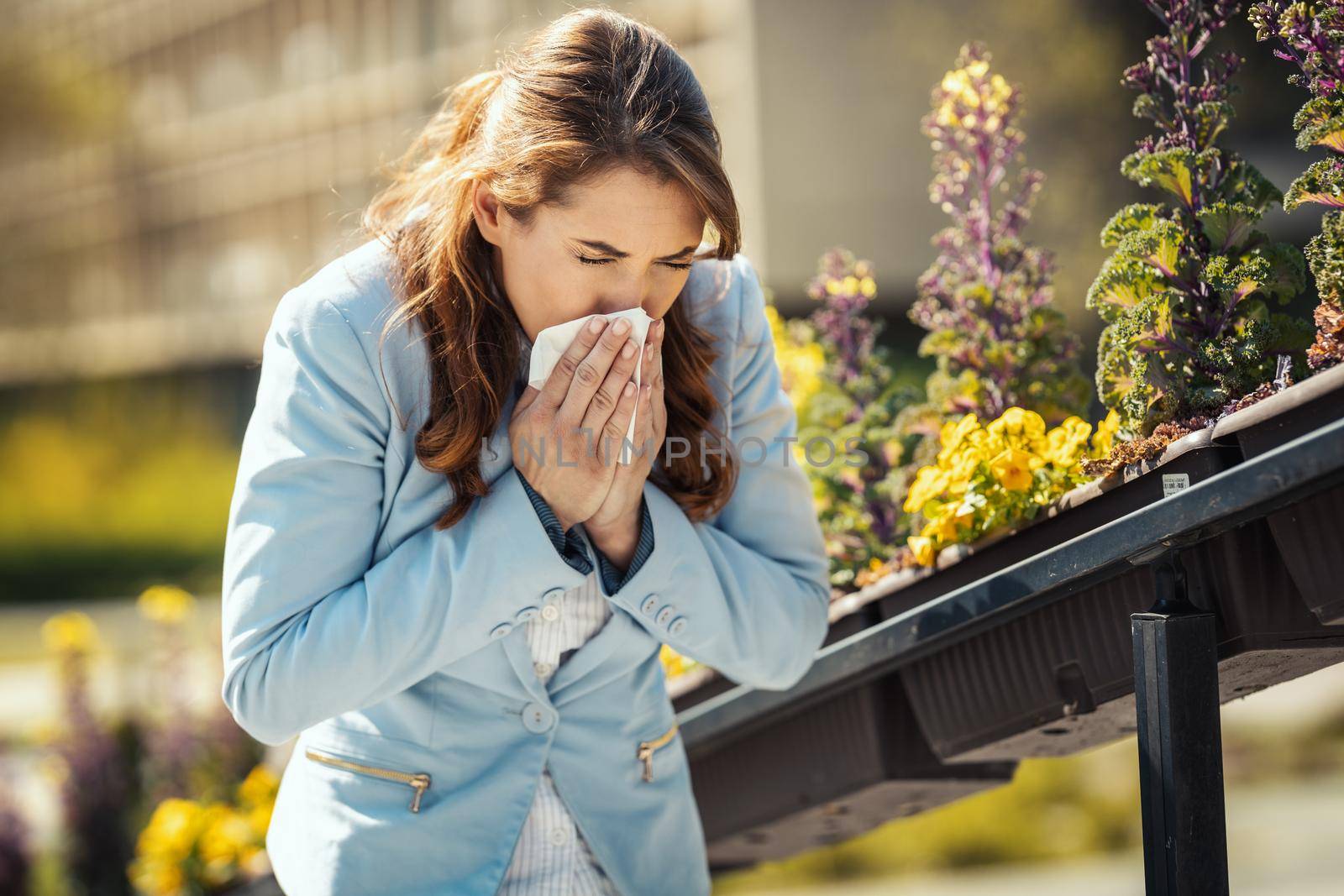 A young business woman blowing her nose out during a break outside due to allergies or colds.