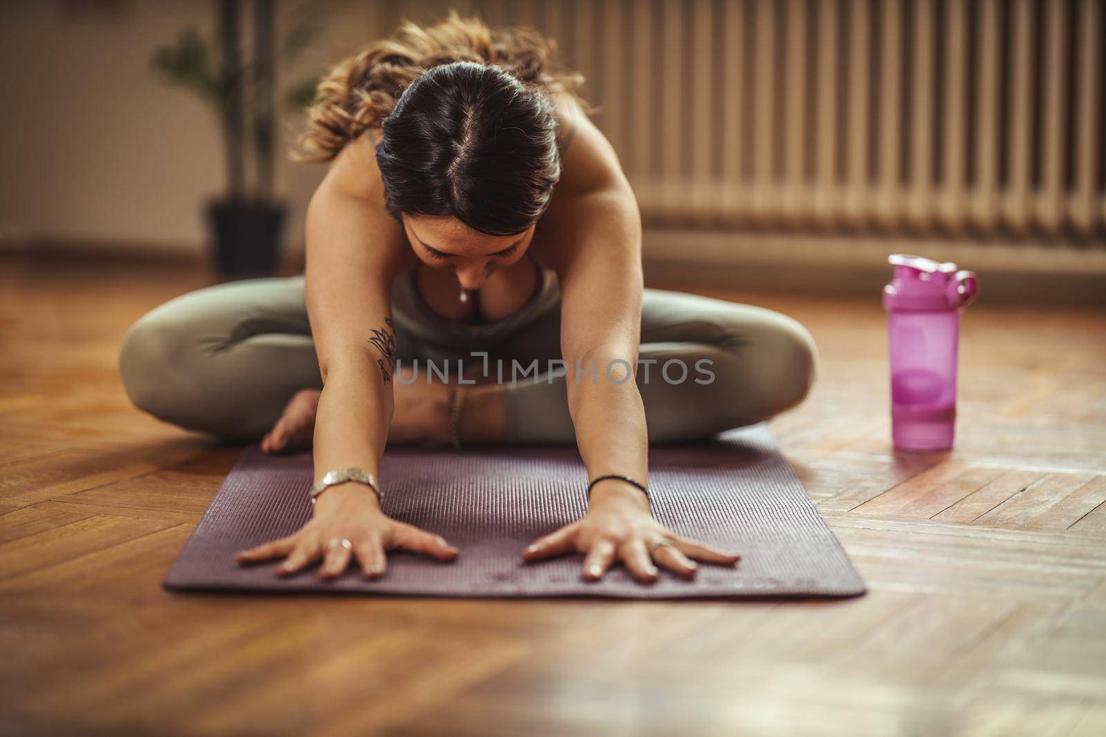 Young woman is doing yoga meditation during coronavirus pandemic in the living room at home. She is meditating on floor mat in morning sunshine.