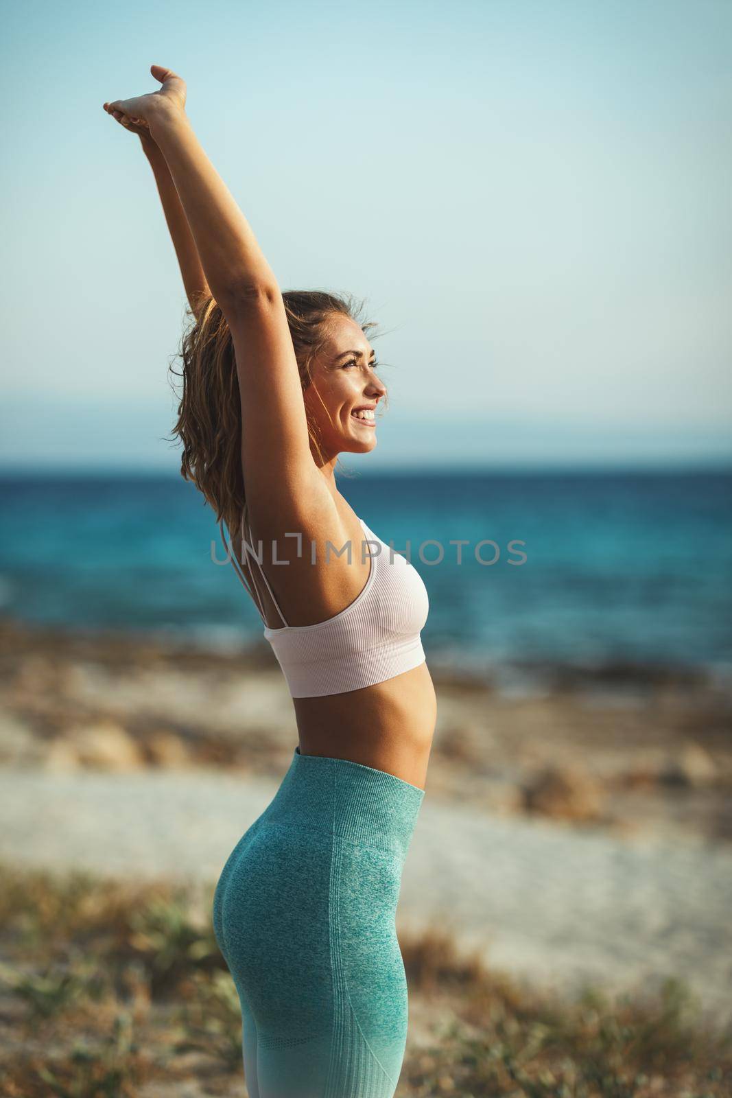 A beautiful young woman is doing stretching exercise at the sea beach in summer sunny day.