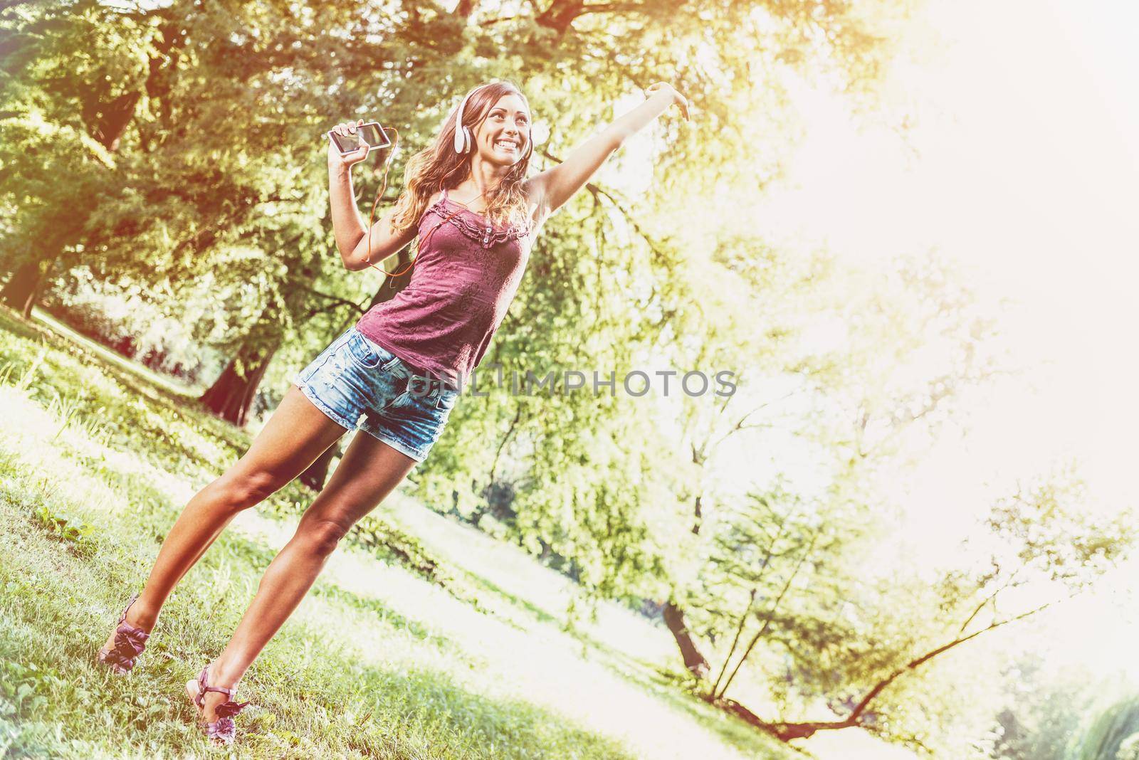Young woman realaxes with headphones,  dancing and listening her favorite song in the park.