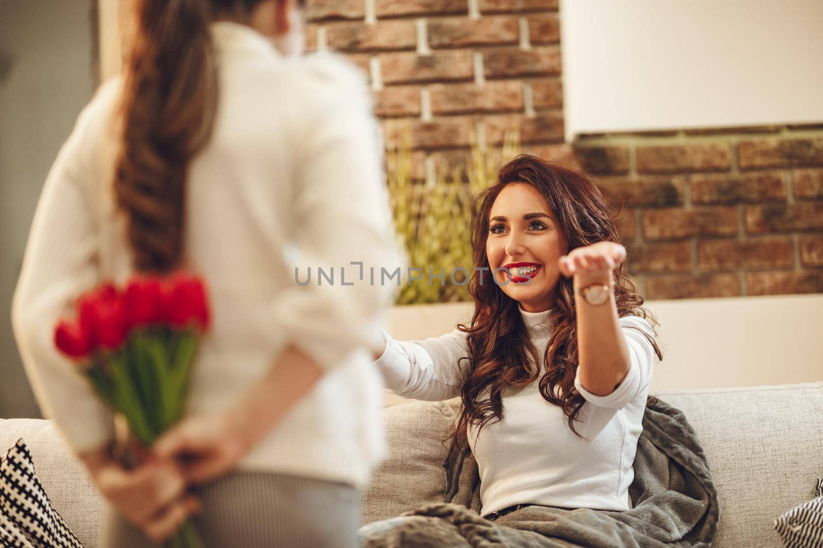 Little daughter is holding nice flowers for her amazed cheerful joyful charming mom congratulates mother's day to her.