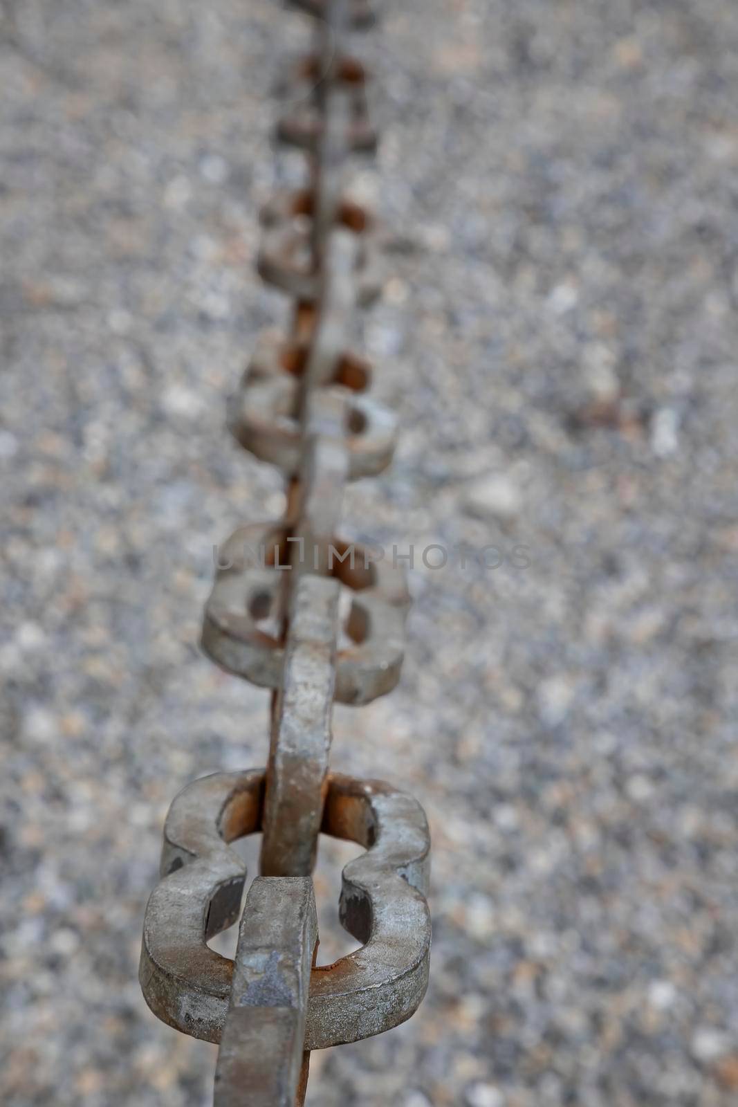 A light gray metal chain made of steel and showing its age is seen up close as it hangs above the broken stone ballast. Selective focus.Vertical view by EdVal