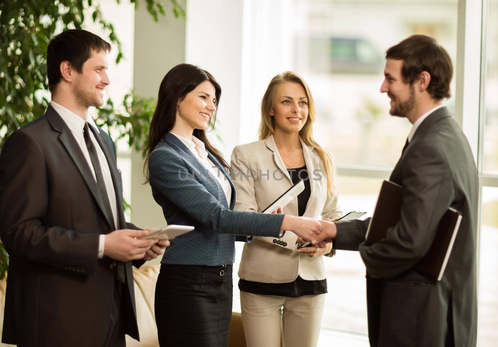 Group of business people congratulating their handshaking colleagues after signing contract