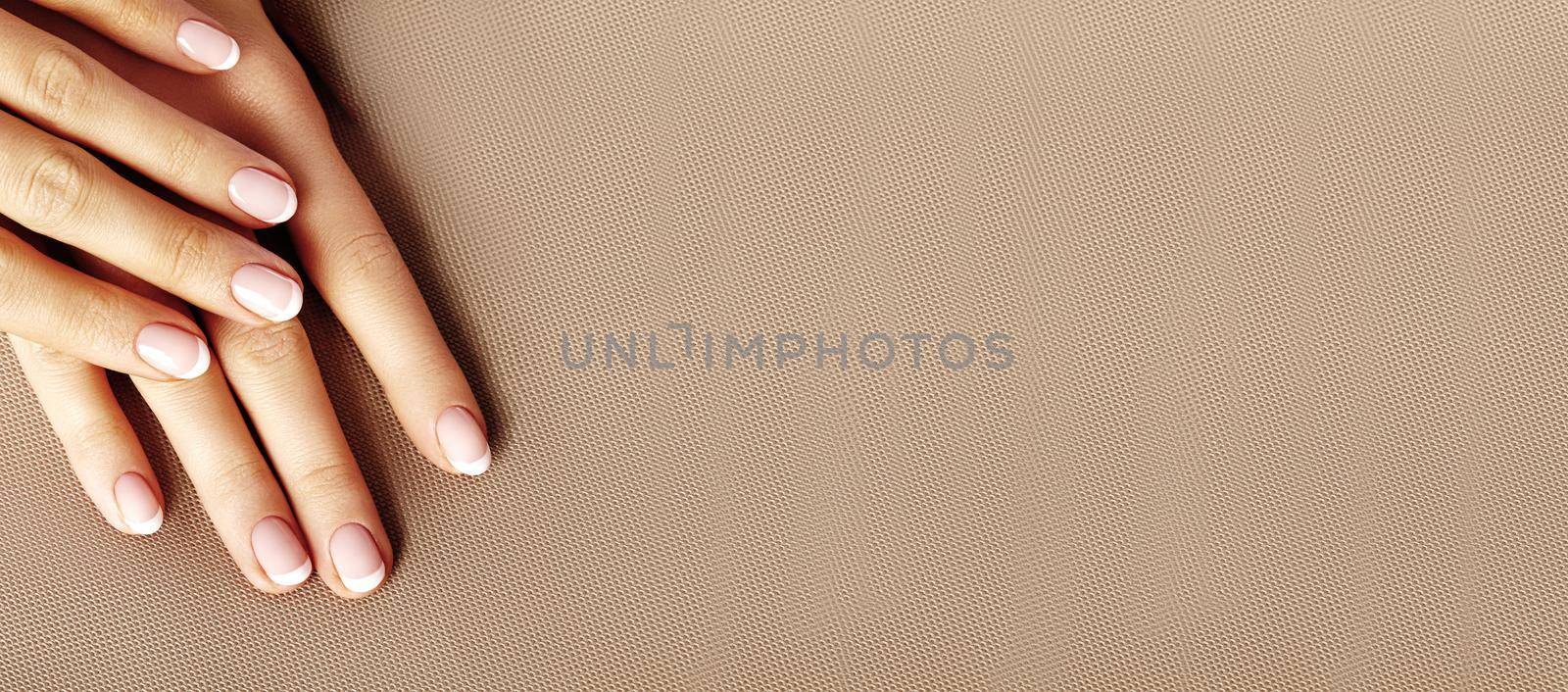 Young Female Palm on beige background. Beautiful Glamour Manicure. French Style. Nail polish. Care about Hands and Nails, clean Skin