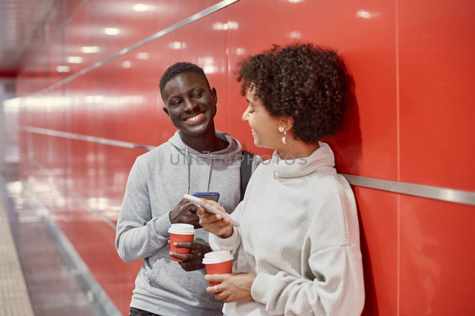 young people with smartphones and takeaway coffee waiting for the subway train . close-up.