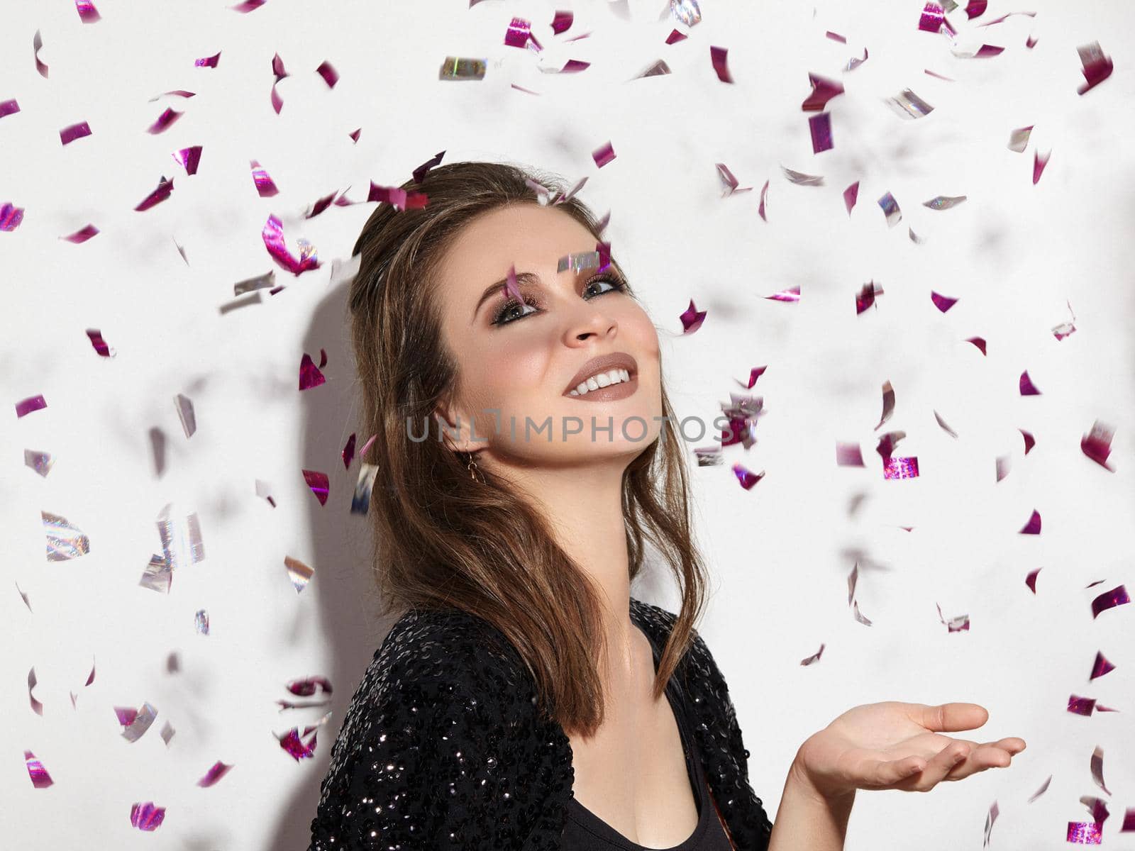Party Time. Beautiful Happy Woman Smiling. Christmas Style in Confetti. Shiny Celebrate Look with Bright Fashion Make-up. Sexy Evening Makeup