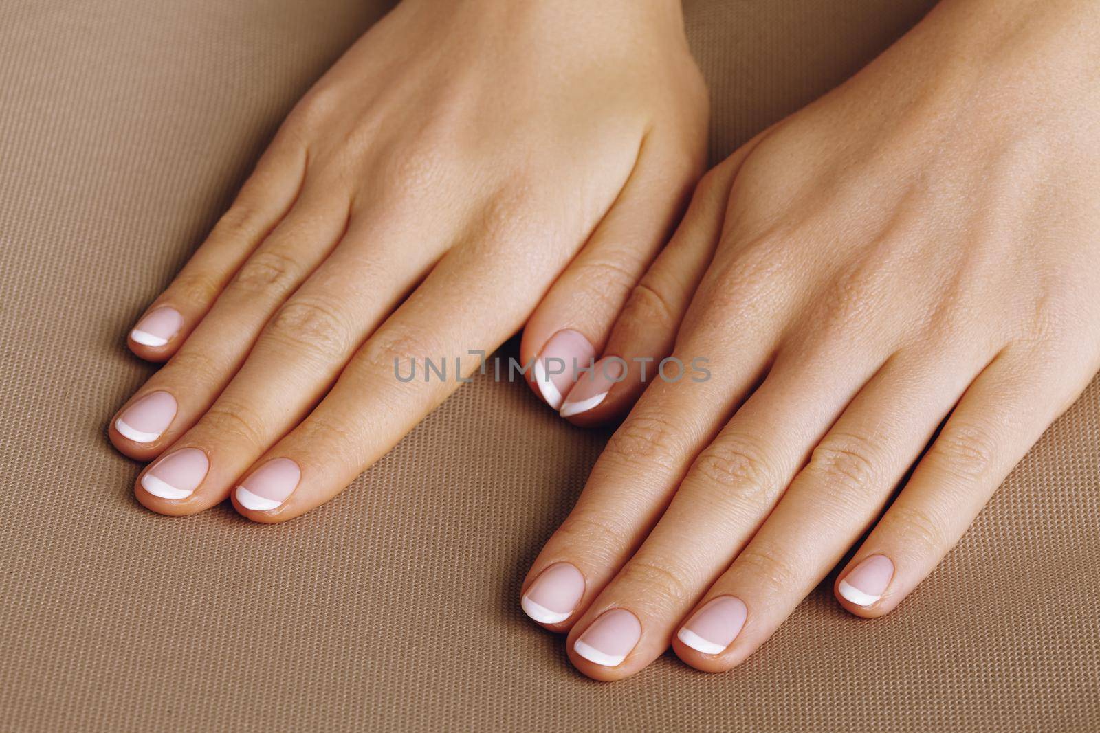 Young Female Palm on beige background. Beautiful Glamour Manicure. French Style. Nail polish. Care about Hands and Nails, clean Skin